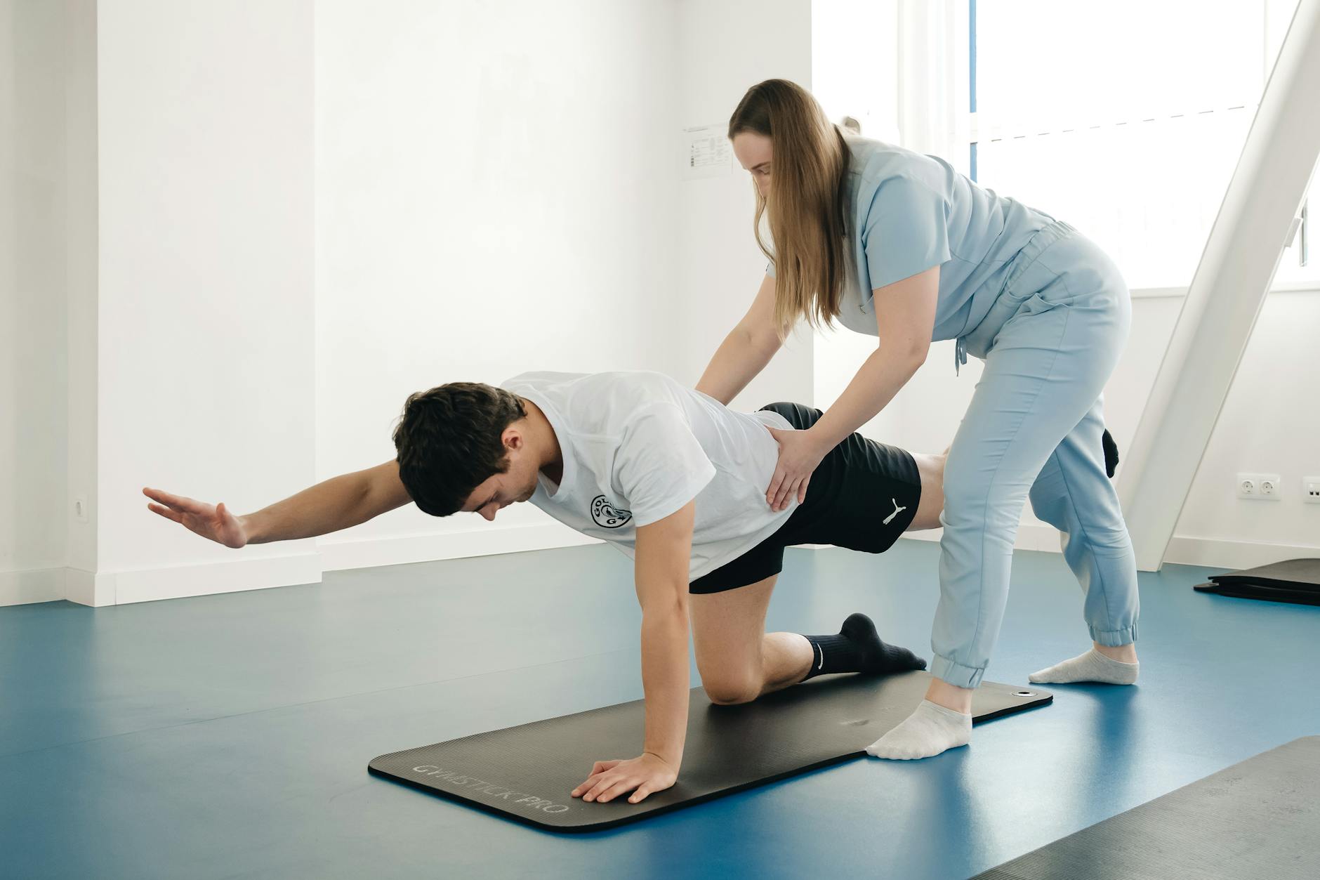 Fizjoterapeuta koryguje ćwiczenie pacjenta na macie w siłowni