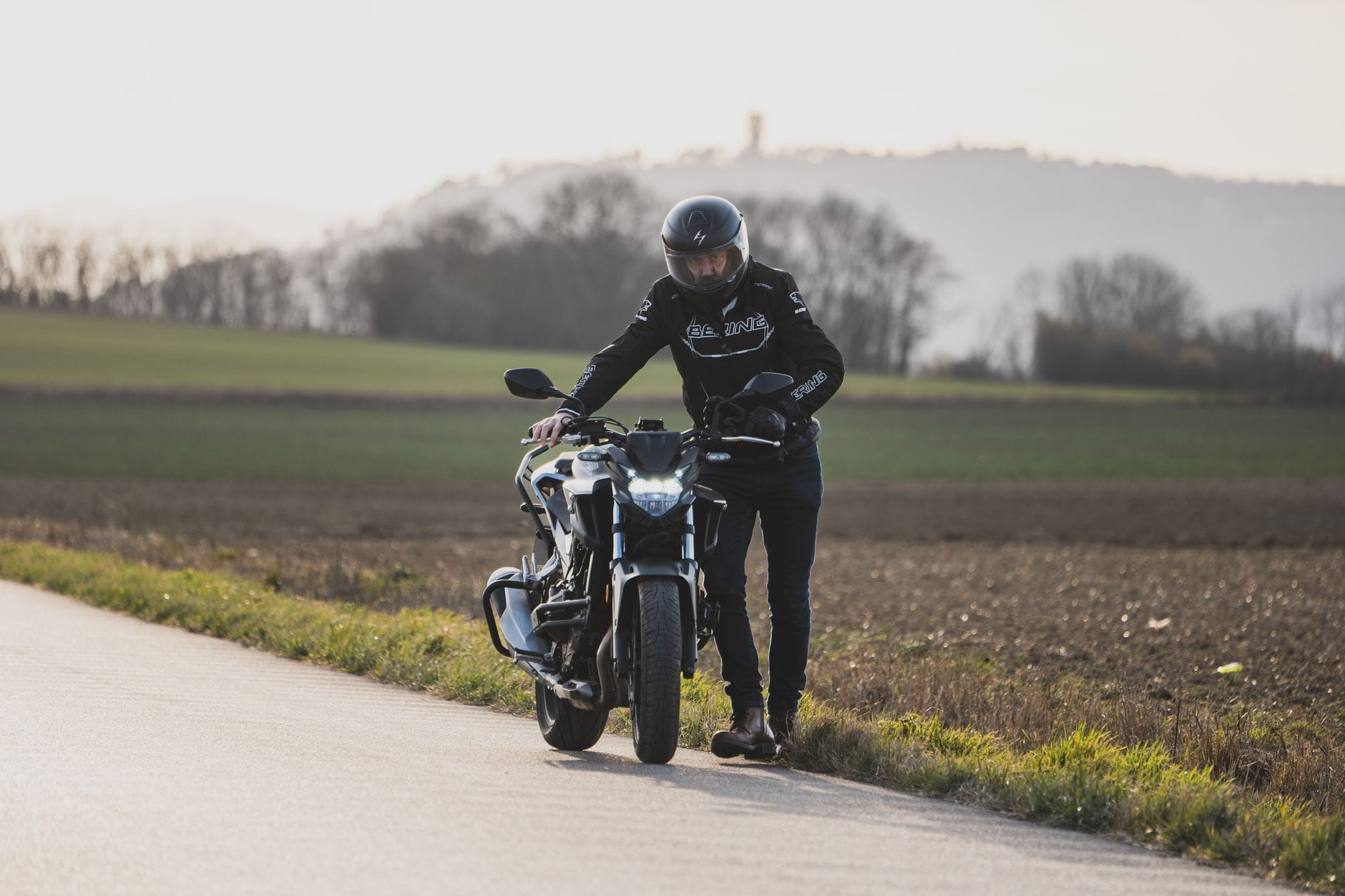Motocyklista w kasku stoi przy motocyklu na wiejskim poboczu drogi
