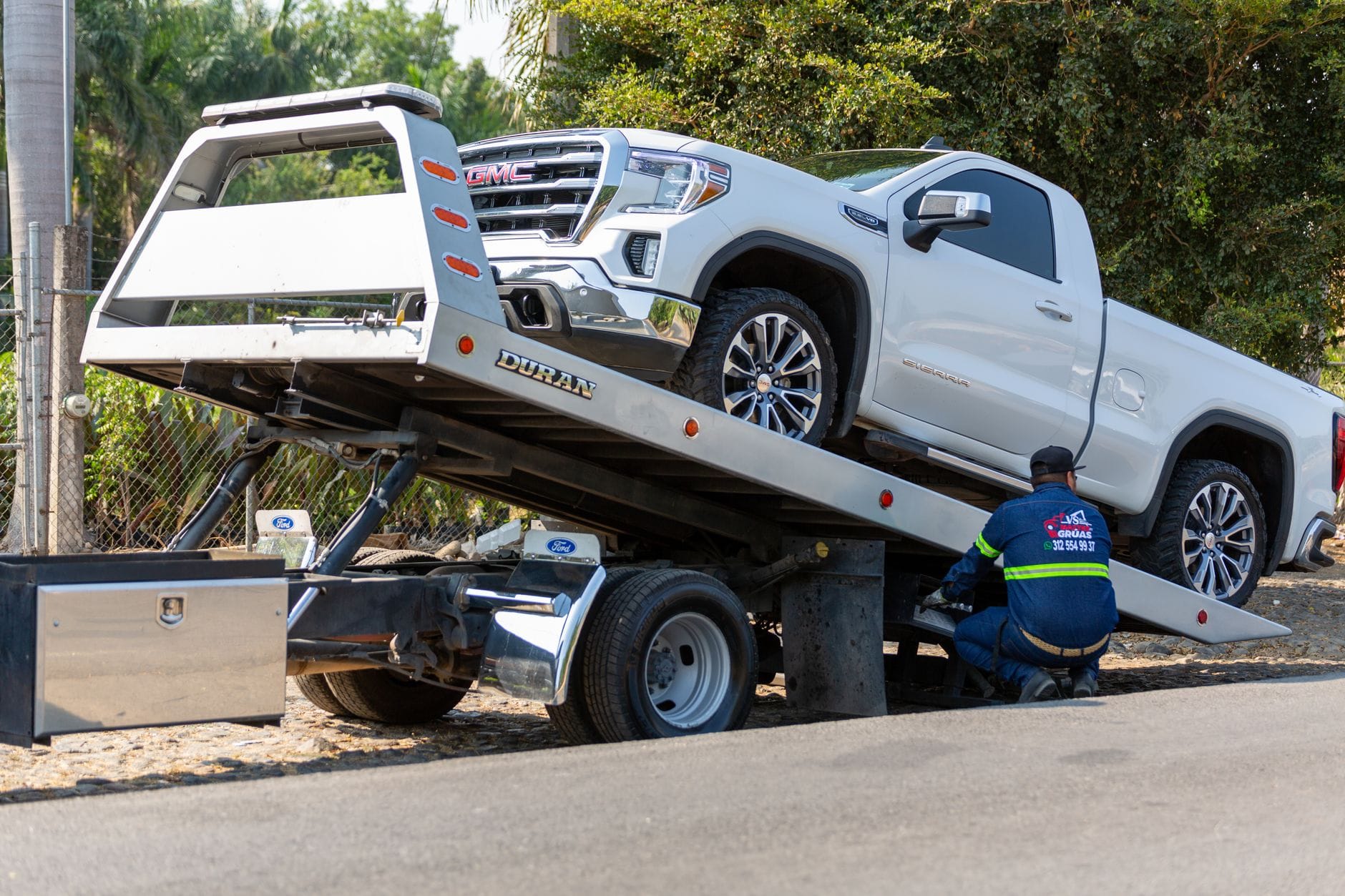 Operator lawety ładuje biały pickup GMC na ulicy w dzień