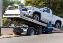 Operator pomocy drogowej ładuje biały pickup GMC na lawetę